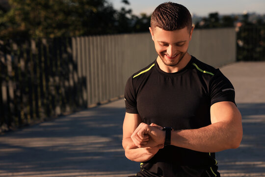 Attractive happy man checking pulse after training outdoors. Space for text