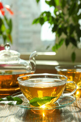 Fresh green tea in glass cups, leaves and teapot on wooden table