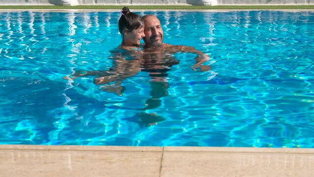 Father hold her daughter in water pool. A cute dad learn to swim her daughter in the swimming pool at hotel during summer vacation.