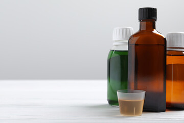 Bottles of syrup and measuring cup on white table against light grey background, space for text....