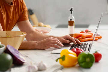Man making dinner while watching online cooking course via laptop in kitchen, closeup