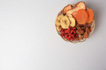 Wicker basket with different dried fruits on white background, top view. Space for text