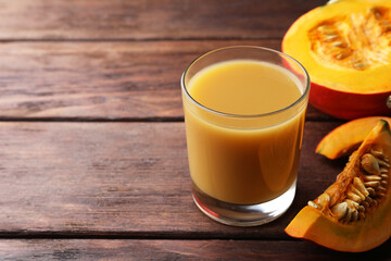 Tasty pumpkin juice in glass and cut pumpkin on wooden table. Space for text