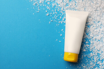 Tube of hand cream and decorative snow on light blue background, flat lay with space for text. Winter skin care