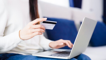 Young asian woman sitting on sofa in living room, makes online banking payments through the internet from bank card on computer laptop. Shopping online on notebook with credit card