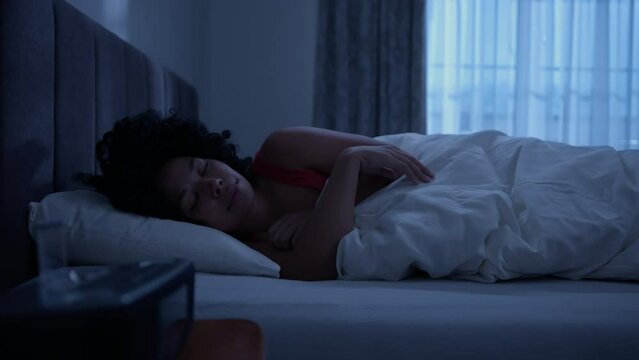 Bedtime rest recreation. Happy relaxed African woman lying in cozy comfortable bed with turned off light, woman of color smiling while dreaming in dark bedroom with blue moonlight. Good night 4K