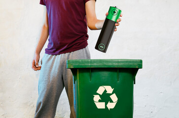 AA battery recycling concept, phot manipulated image. man holding big battery over garbage bin with...