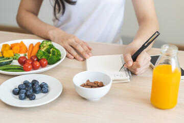 Diet, Dieting hand of asian young woman, girl write diet plan nutrition on table is different food ingredients in the green. Nutritionist of healthy, nutrition of weight loss, health care people.