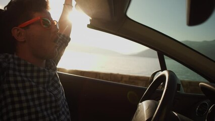 A young men in a shirt rides a convertible along the seashore in the mountains, enjoys the wind with his hand. Vacation, car purchase and car rental