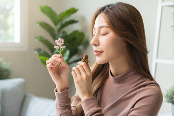 Aromatherapy, cute asian young woman, girl holding flower, bottle of essential perfume oil, enjoying smell fragrance of herbal from medicine natural organic at home.Therapy treatment, beauty skin care - obrazy, fototapety, plakaty
