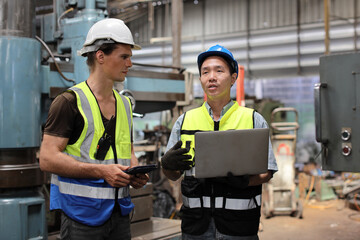 Fototapeta premium Technician engineer in protective uniform with hardhat standing and teaching apprentices or colleague worker to use computerized machine control at heavy industry manufacturing factory