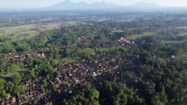 Dense build villages surround with green jungles, rice fields seen next, mountains silhouetted on back. Aerial shot of Bali upland at north of Ubud town, deep shadows and nice view in sunny morning