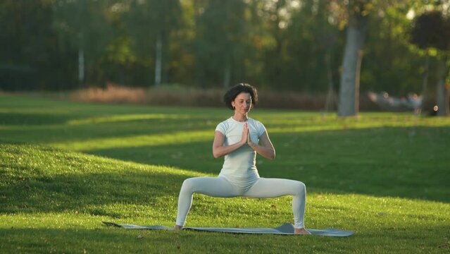 Active, healthy, caucasian woman stretching on a mat in grassy meadow. Sporty, fit girl meditating in city park with lush natural environment. High quality 4k footage