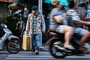 Asian poverty homeless man hold dragging large suitcase walk across the crosswalk in city. poor man live in slump no job, pity aged person problem from financial crisis unemployment without family