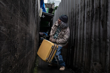 Asian homeless man dragging large suitcase in a narrow alley for to find rest, no home live on...