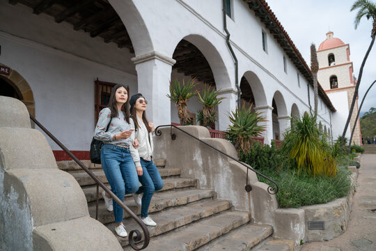 full length of two asian chinese female backpackers walking down stairs near the archway as while exploring the grounds of old mission santa Barbara in California usa