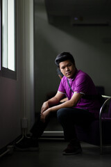 Portrait of asian man black hair wear purple shirt sitting in shadow in front of mirror window light looking outside