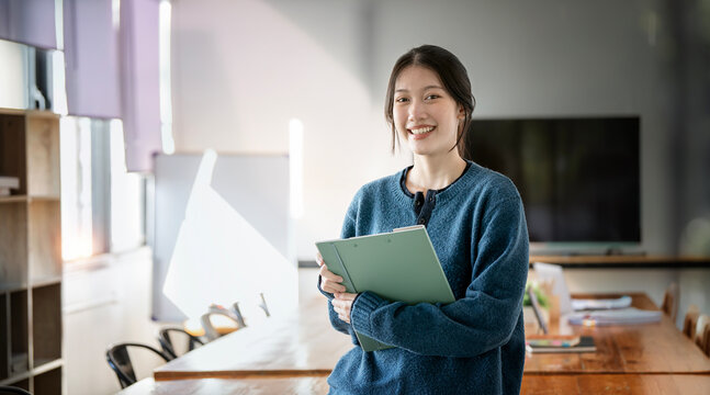 Young Asian businesswoman looking at camera holding file folder at office.