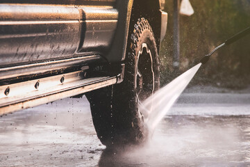 Washing offroader car at a self-service car wash with a high-pressure water jet after off-road...
