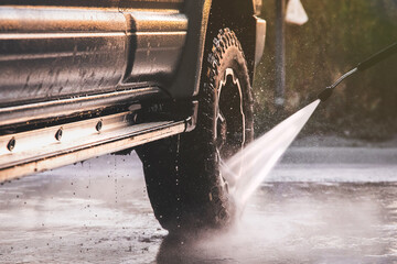 Washing offroader car at a self-service car wash with a high-pressure water jet after off-road driving.