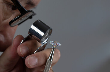 Jeweller hands with natural cut and polished diamonds, jeweller tools, loupe, tweezers, white diamonds.