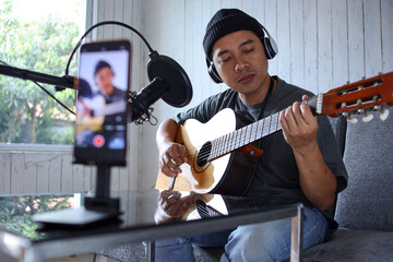 Asian influencer playing guitar during podcast or live video broadcast for the audience from the...