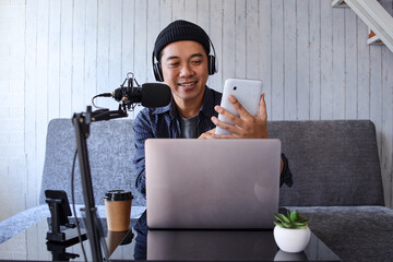 Asian man recording a podcast on her laptop computer with headphones and a microphone from home studio