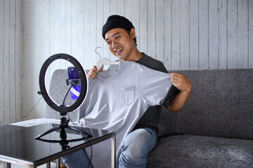 Asian seller reviewing product and talking to camera live recording video on social network at...