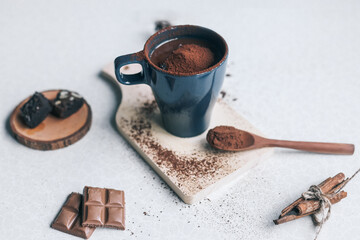 Cup of hot chocolate and pieces of chocolate on light concrete background