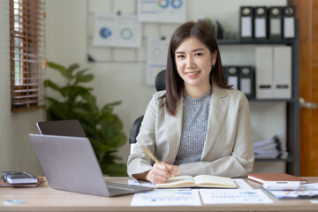 Attractive Asian businesswoman with laptop in office With a bright smile and looking at the camera.