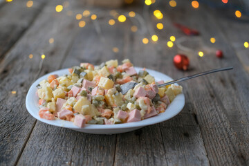 Homemade New Year is Olivier salad on a wooden background. Plate with a spoon of traditional Russian Christmas salad.