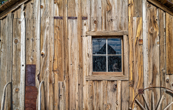 An old wagon wheel rests under the window of an rustic cabin wall