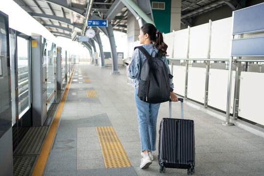 Young female traveler walking with black suitcase at modern transport stop outdoors, back view The concept of urban transport and travel.