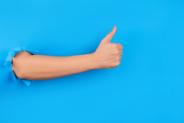 Female hand showing thumb up as sign of approval or agreement isolated over blue studio background. Best choice concept. Hole in wal.