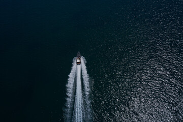 Drone view of a boat sailing. Top view of a white boat sailing to the blue sea. Motor performance boat in the sea. Large white boat fast movement on blue water aerial view.