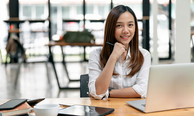 Plakat Portrait of happy business woman sitting at workplace in office. Young attractive female worker using modern laptop, looking at camera.