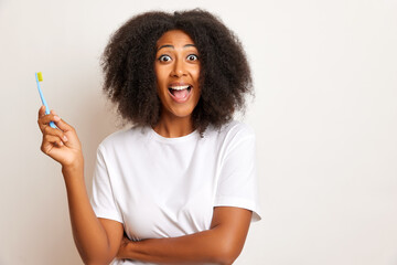 Horizontal shot of curly haired woman holds a toothbrush and widely smiles, copy space, wears casual white T-shirt, isolated over white background