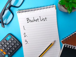 Calculator,pencil and notebook with the word Bucket List on blue background.