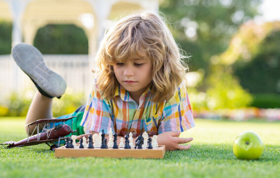 Kid Thinking About Chess Laying On Grass In Summer Park. The Concept Of Learning And Growing Children. Chess, Success And Winning. Outdoor Game, Kids Hobby And Lifestyle.