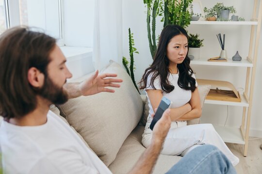 A man looks at the phone screen during an argument with his girlfriend. The angry and hurt woman looks in his direction and is sad. Family discord at home, phone addiction