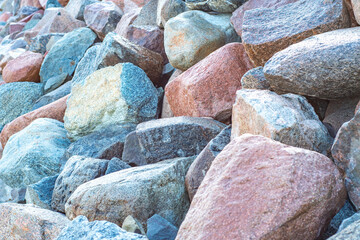 Close-up of a pile of large granite stones with a fine texture. Background with a protective embankment of pebbles on the beach.