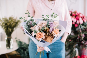 Very nice young woman holding big and beautiful bouquet of fresh carnations, roses, anthurium and eucalyptus in peach, pastel purple, gold colors, cropped photo, bouquet close up