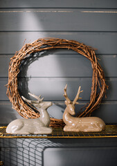 Two ceramic deers and hand made wooden wreath on the rustic grey wall background, vertical photo