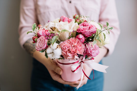 Very nice young woman holding beautiful composition in a small pink bucket of fresh roses, cotton, carnations, eustoma in pink colors, cropped photo, bouquet close up