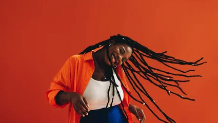 Gordijnen Young, fashionable black woman celebrates and enjoys herself with a hair flip, dancing and smiling in a vibrant studio setting © Jacob Lund