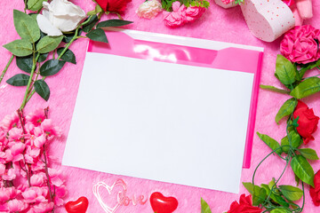 White blank A4 paper on the to of pink envelope surrounded by valentine themed decorations