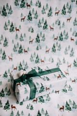 Beautiful gift wrapped in a festive paper with deer and spruce trees print on the same paper background, vertical photo