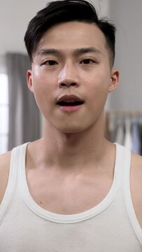 Vertical Video: front shot of asian male walking near and looking at camera like mirror beating his chest and making pep talk to himself with gestures in the morning at home.