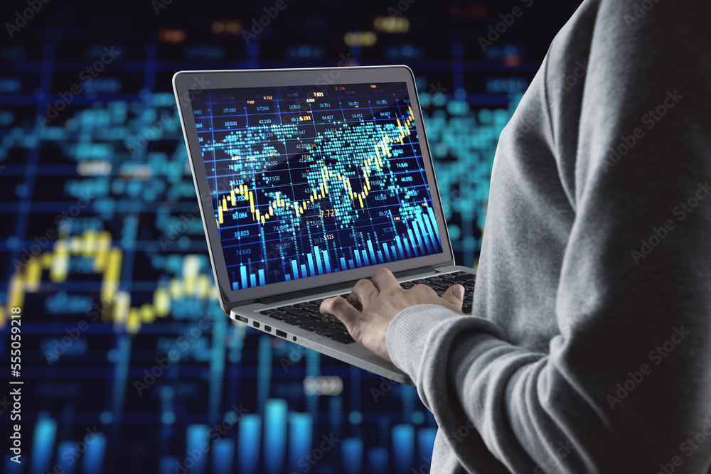 Poster Close up of hand holding and using laptop with glowing forex index chart/graph on dark background. Trade, finance and invest concept.