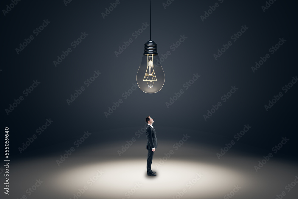 Aufkleber Creative idea and solution concept with businessman looking up at the ceiling with a big hanging light bulb on abstract dark background